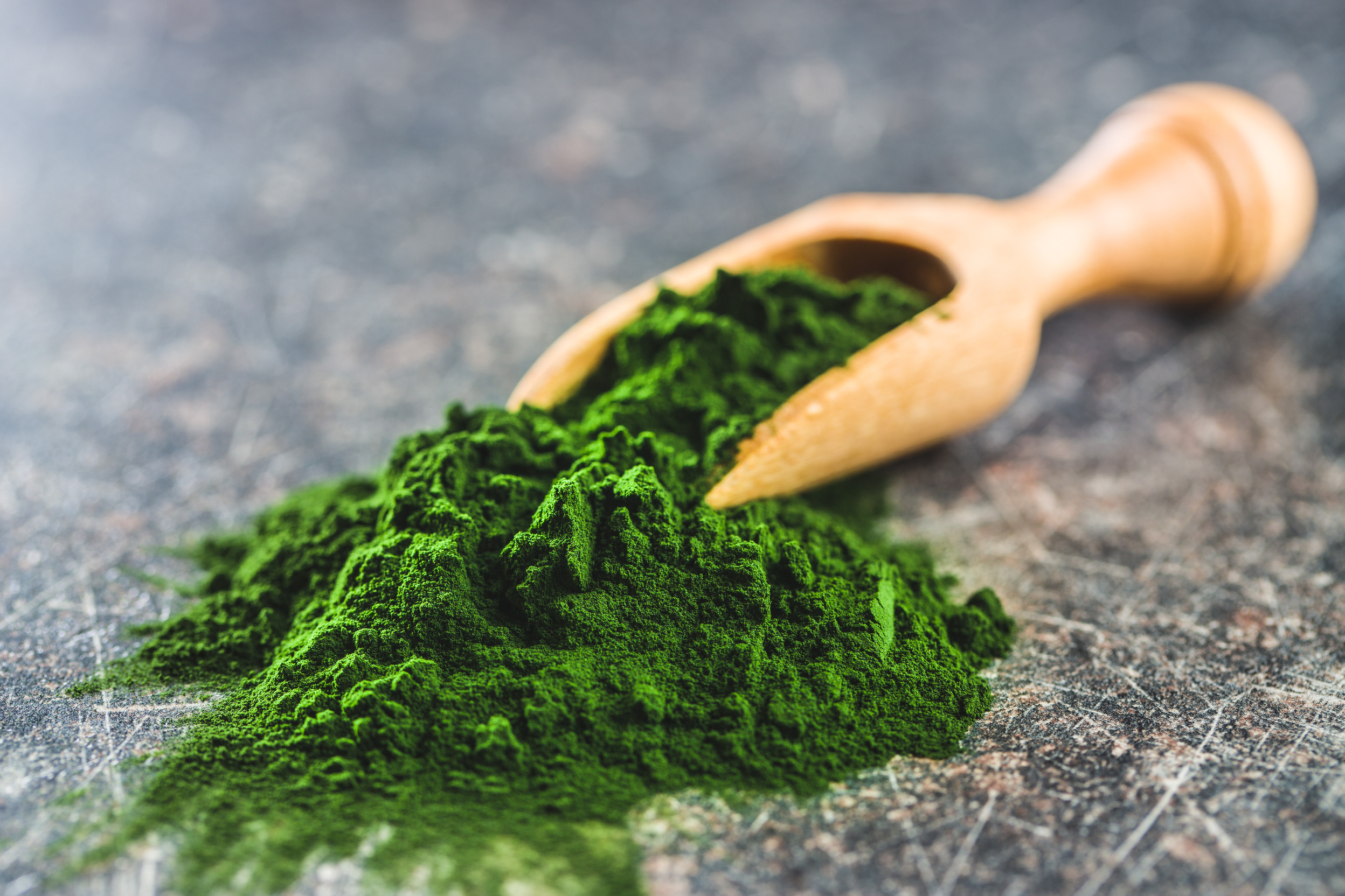 Green chlorella powder in wooden scoop.